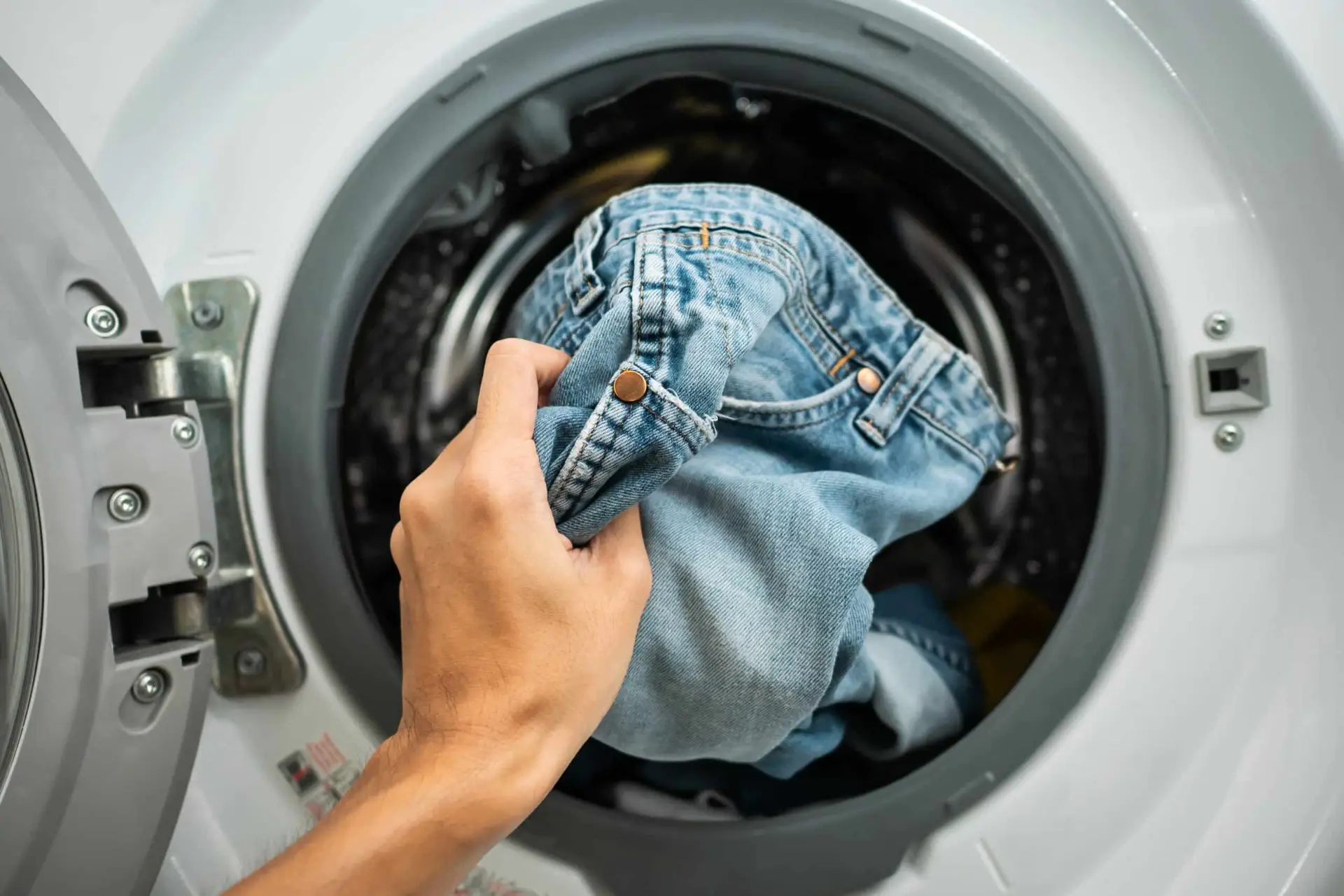 a hand holding a blue jeans in a washing machine